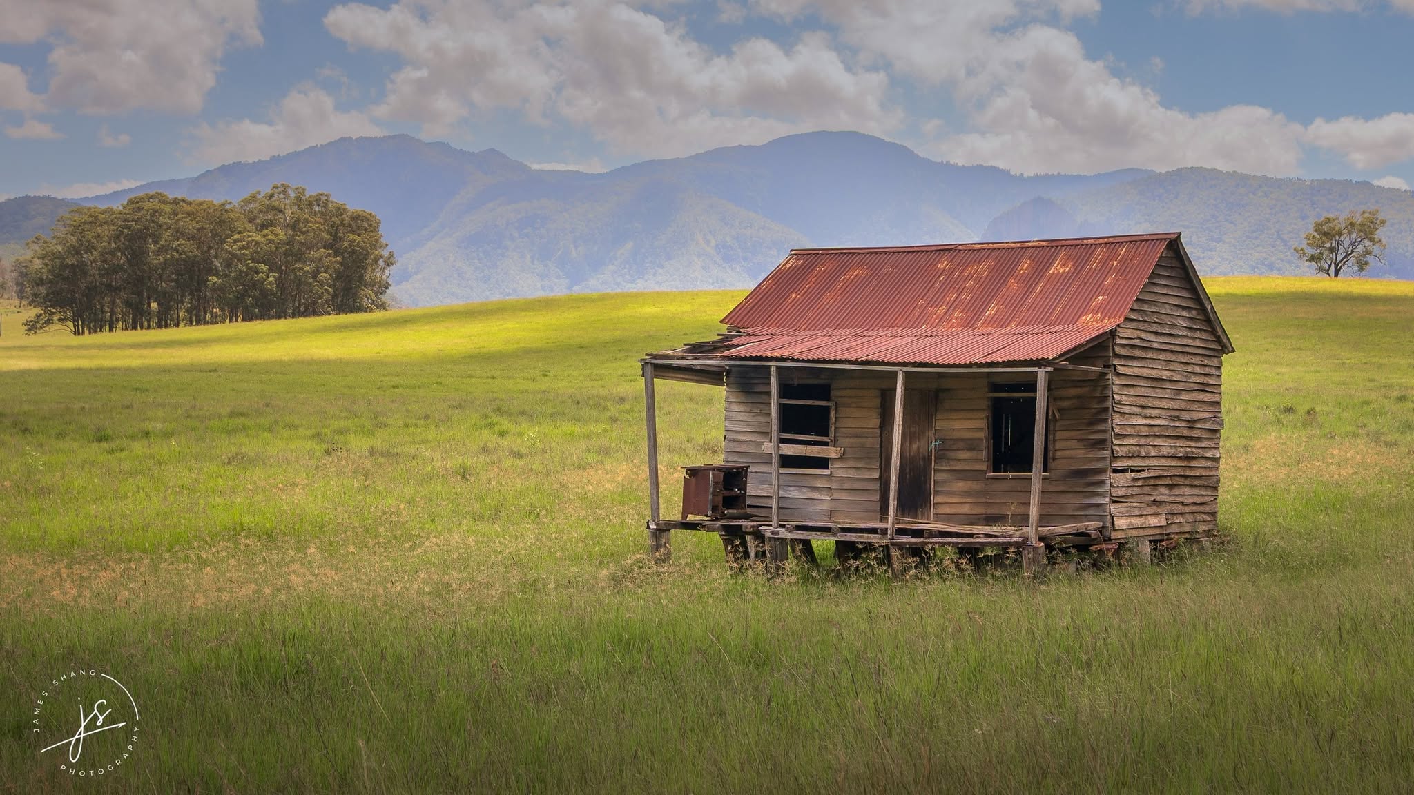 Old timber hut against green fields and distant mountains